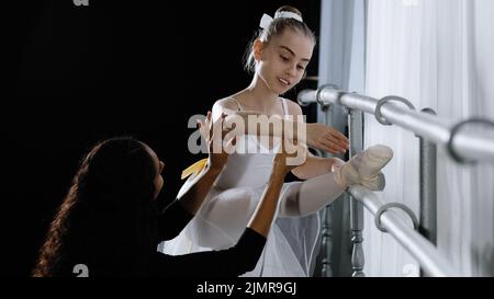 Beginner ballerina in tutu teenage girl listens to advice of adult woman coach to learn to dance together in dancing school near barre. Female teacher Stock Photo