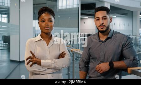 Business people African lady businesswoman and adult Arabian man boss manager standing in office and posing for camera with crossed arms. Two Stock Photo