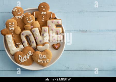 Festive cookies in the form of hearts, letters and gingerbread men in a plate on a blue background. Stock Photo