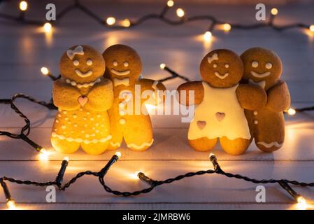 Love concept, two pairs of gingerbread, illuminated with light garlands. Stock Photo