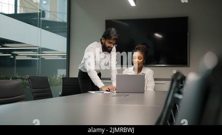Professional Arabian Indian teacher mentor helping African woman new employee teaching intern explaining online project service corporate app using Stock Photo