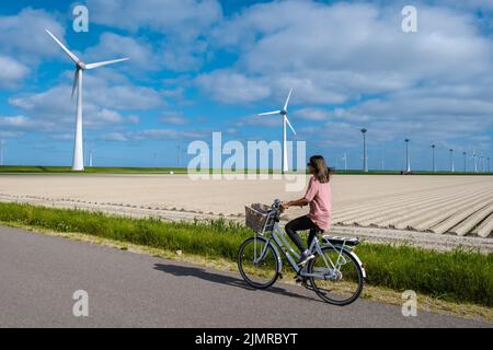 Young woman electric green bike bicycle by windmill farm , windmills isolated on a beautiful bright day Netherlands Flevoland No Stock Photo