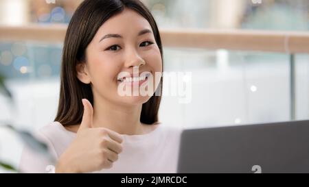 Portrait happy asian business woman portrait posing workplace showing cool thumb up gesture smiling agree super good with positive emotion. Modern Stock Photo