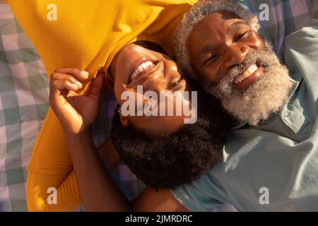 High angle portrait of smiling african american couple lying on blanket at beach on sunny day Stock Photo