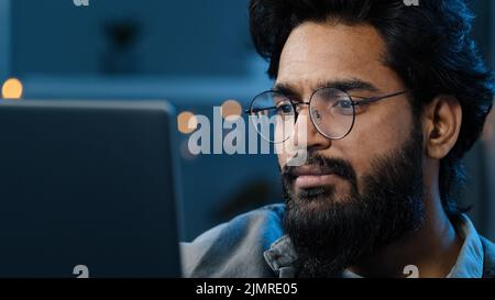 Thoughtful arabian indian bearded adult man thinking of problem solution working on laptop at home doubtful male face in glasses looking at computer s Stock Photo