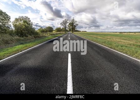 Asphalt road in field under blue cloudy sky Stock Photo