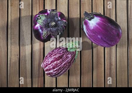 Composition of three round purple eggplants aubergine on wood background Stock Photo