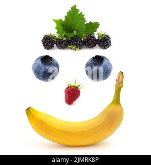 Smile face made of fruits, banana with raspberries and blueberries isolated on white background. Stock Photo