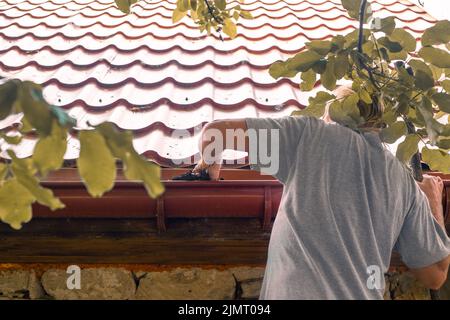A gardener cleans the gutter of a drainpipe from dry leaves. Prevention ...