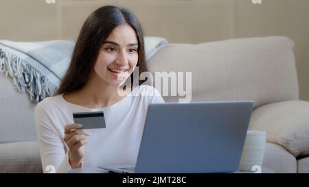 Happy female arabian consumer shopper hold plastic banking card enter numbers for online bank app pay money deposit use credit limit donate for Stock Photo