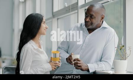 Two diverse age multi-ethnic colleagues businesspeople co-workers partners friends african senior adult man arab young woman standing indoors talk Stock Photo