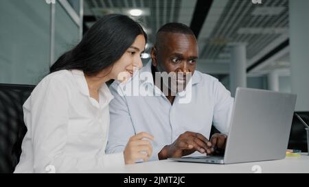 Two diverse colleagues businesspeople african senior man lawyer and arabian woman worker sit in modern co-working office look at laptop consult Stock Photo