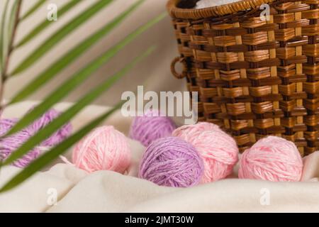 Balls of pink and lilac yarn lie next to a wicker basket. Home needlework. Handmade work. Selective focus Stock Photo