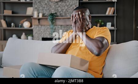 Surprised african adult man unpack parcel box american bachelor homeowner consumer birthday person male buyer get present from internet store delivery Stock Photo