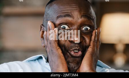 Surprised portrait african american ethnic joyful emotional man businessman 50s male consumer touches face by hands feel happiness triumph good shock Stock Photo