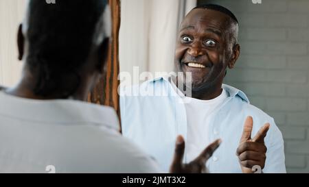 Close up senior comical man look in mirror reflection african american retiree confident 50s unshaven emotional adult businessman pointing forefinger Stock Photo