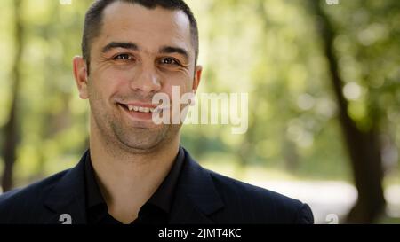 Portrait joyful friendly caucasian arab businessman successful salesman clever freelancer wears formal suit stands in urban park looks at side Stock Photo
