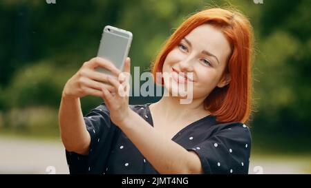 Beautiful caucasian redhead girl stylish model woman female blogger takes selfie photo self-admiration records video lifestyle blog on modern Stock Photo