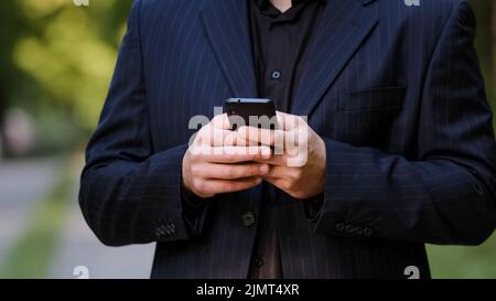 Close up male hands unknown man in black formal suit hold smartphone chatting in social media use mobile app chat texting message search information Stock Photo
