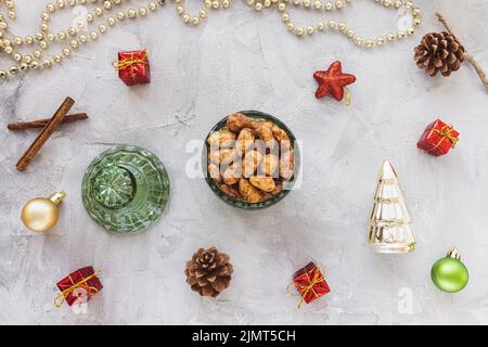 Candied or sugared almonds with honey and cinnamon in bowl on gray with Christmas decoration background. Traditional Christmas sweets for holidays. Top view, copy space Stock Photo