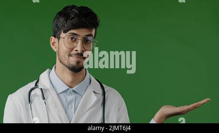 Arab indian guy young male doctor practitioner man hold copy space on palm pointing at workspace mockup promo place for advertisement image offer Stock Photo