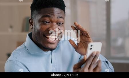 Happy young african american guy businessman handsome entrepreneur man worker hold smartphone talk by video call greeting have virtual meeting chat Stock Photo