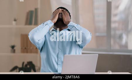 Frustrated shocked african businessman american adult man student work on computer make error mistake feels stress upset with bad news failure e Stock Photo