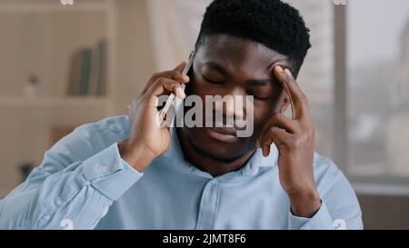 African man businessman american male employee worker answer incoming call talking on phone in home office disappointed frustrated young guy receiving Stock Photo