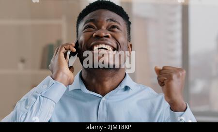 African american businessman professional male analyst man answer incoming call talking on phone in home office happy shocked amazed young guy get Stock Photo