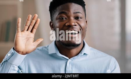 African handsome friendly man american young guy blogger teacher coach say hello look at camera wave hand greeting record lifestyle blog educational Stock Photo