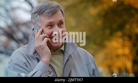 Portrait mature elderly man pensioner communicate remotely using modern smartphone talking family or friends order delivery happy old senior laughing Stock Photo