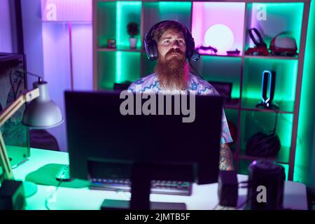 Young redhead man streamer playing video game using computer at gaming room Stock Photo