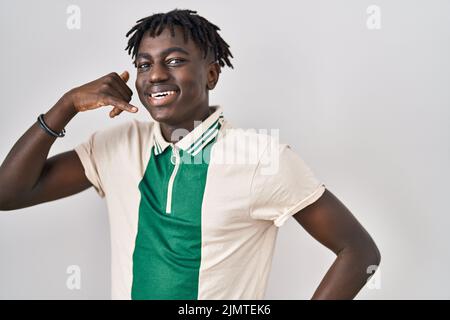 African man with dreadlocks standing over isolated background smiling doing phone gesture with hand and fingers like talking on the telephone. communi Stock Photo