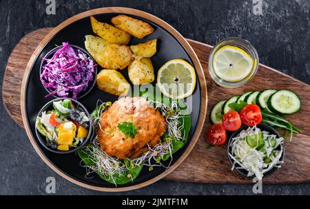 Pulled chicken cutlet coated with breadcrumbs with potatoes and vegetable salads Stock Photo