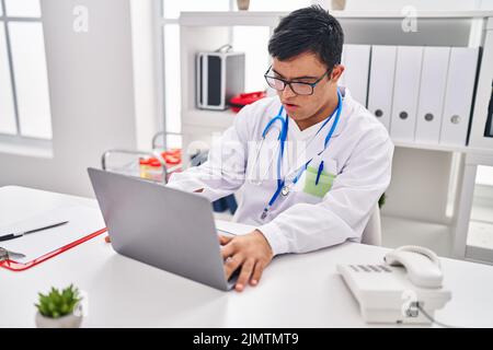 Down syndrome man wearing doctor uniform using laptop working at clinic Stock Photo