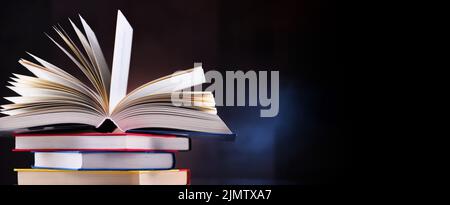 A composition with an open hardcover book lying on a stack of other books Stock Photo