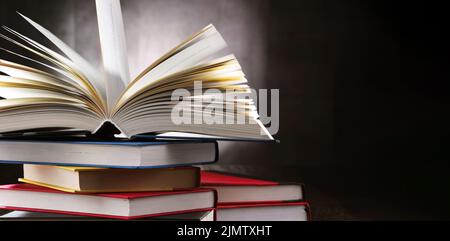A composition with an open book lying on a stack of other books Stock Photo