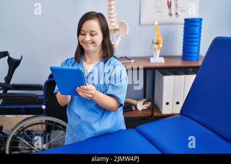 Down syndrome woman wearing physiotherapy uniform using touchpad at physiotherapist clinic Stock Photo