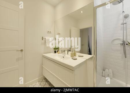 Bathroom with one-piece white porcelain sink, large frameless wall mirror, wooden cabinet with drawers and glass door shower stall Stock Photo