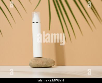 White plastic cosmetic bottle with dispenser and transparent cap on brown background. Packaging for cream, fluid and gel Stock Photo