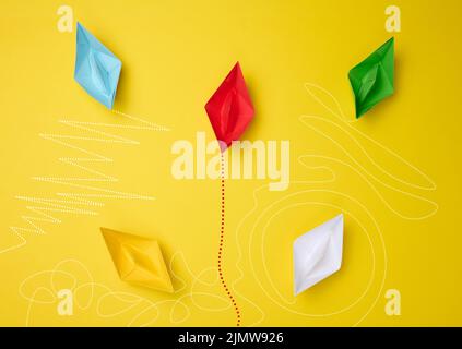 Paper boats with different trajectories on a yellow background. The concept of extraordinary thinking Stock Photo