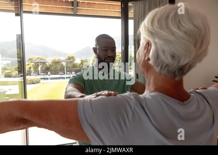 African american male physiotherapist helping caucasian senior woman to perform stretching exercise Stock Photo