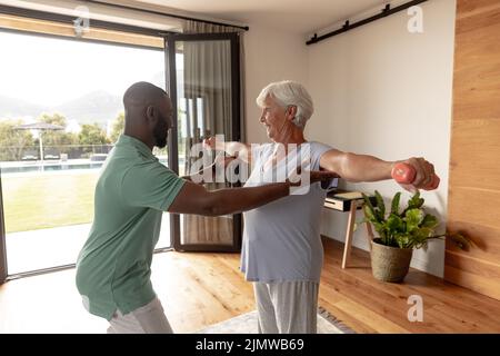 African american male physiotherapist helping caucasian senior woman to do exercise with dumbbells Stock Photo