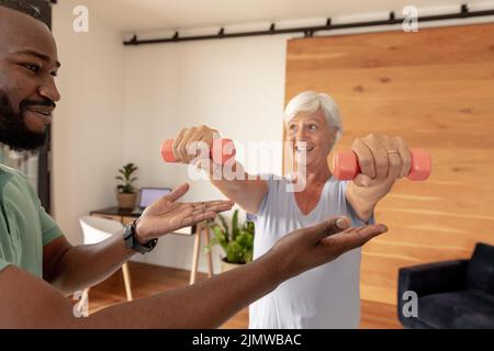 African american male physiotherapist helping caucasian senior woman to do exercise with dumbbells Stock Photo