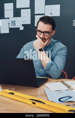 Putting his creative mind to work. a handsome young male architect looking thoughtful while working on a laptop in his office. Stock Photo