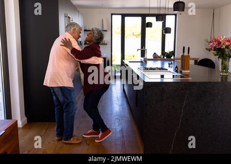Side view of happy romantic multiracial senior couple dancing in kitchen at retirement home Stock Photo