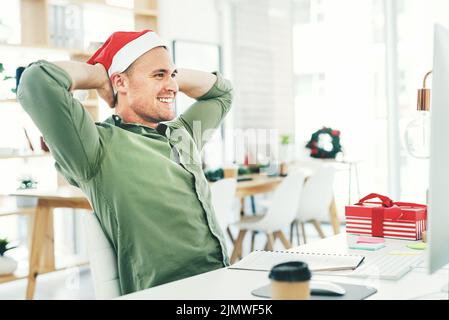 Im watching everything fall into place. a young businessman relaxing with his hands behind his head while working in his office on Christmas Eve. Stock Photo