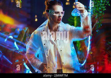 modern scientist woman in lab coat with flask and futuristic goggles in metaverse. Stock Photo