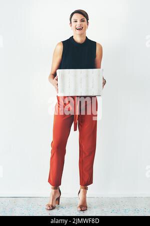 Who doesnt love getting spoiled. Full length shot of an attractive young woman holding a wrapped present against a grey background. Stock Photo