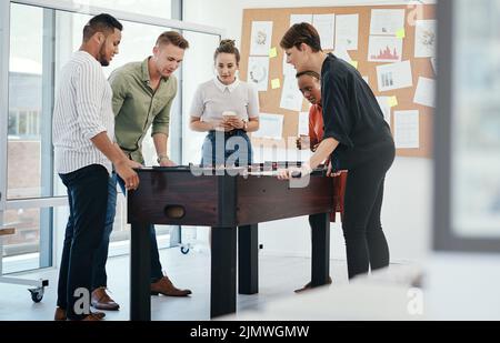 Getting some moral support from colleagues. a diverse group of businesspeople standing together and bonding over a game of foosball in the office. Stock Photo